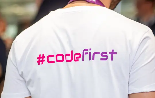 A person facing away. They have a shirt which says 'hashtag code first'